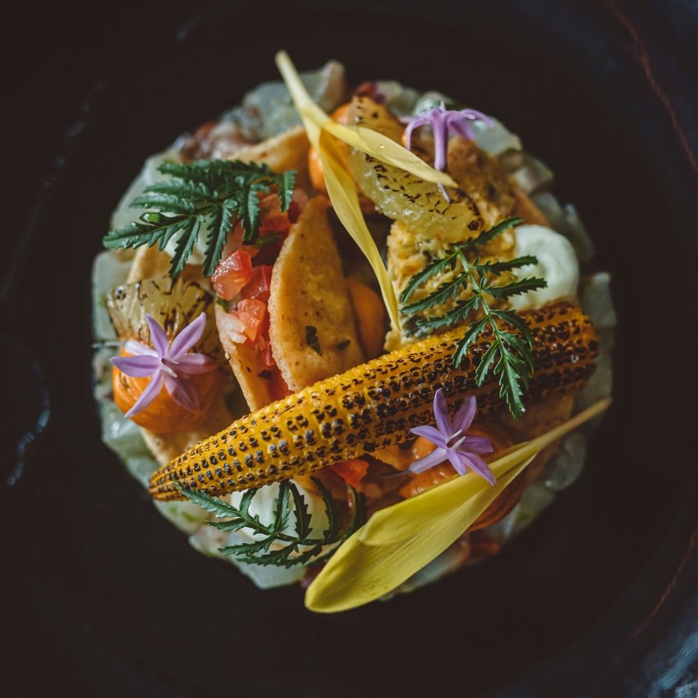 Gerecht Met Gegrilde Maïskolf Groenten Kruiden En Eetbare Bloemen In Een Donker Bord Van Bovenaf Gefotografeerd