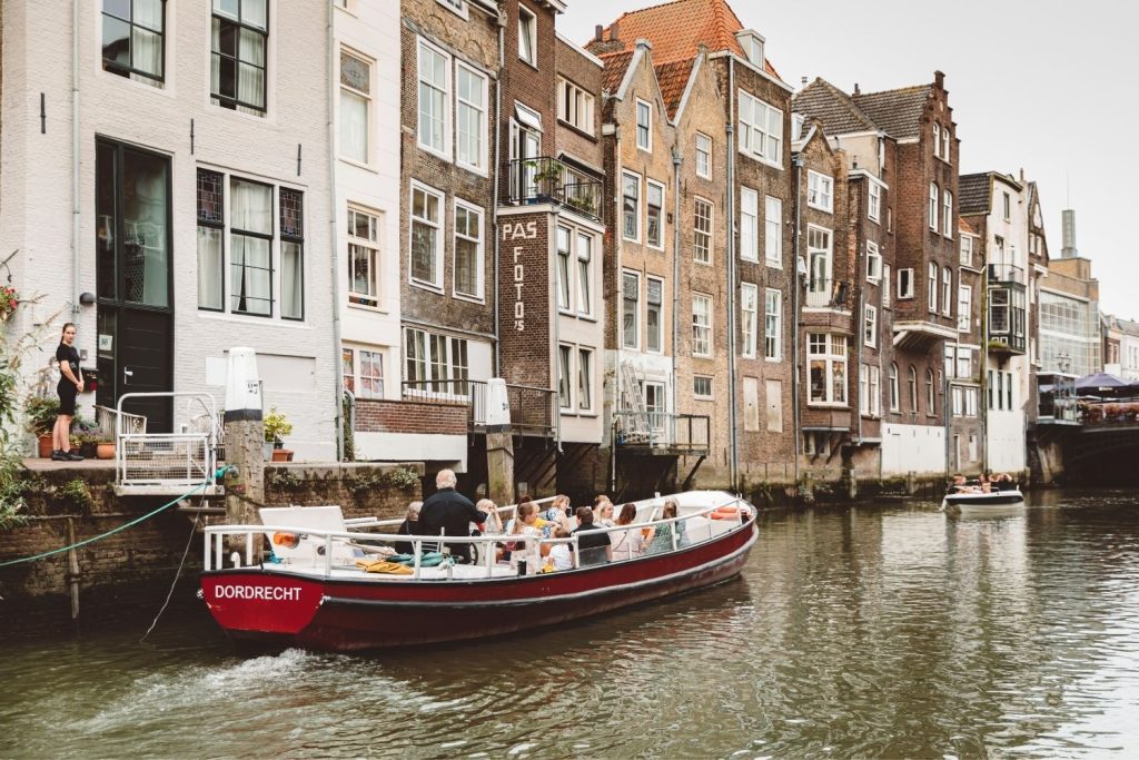 Rode Rondvaartboot 'Dordrecht' Met Passagiers Op Een Gracht Langs Historische Gevelpanden Rode Rondvaartboot 'Dordrecht' Met Passagiers Op Een Gracht Langs Historische Gevelpanden